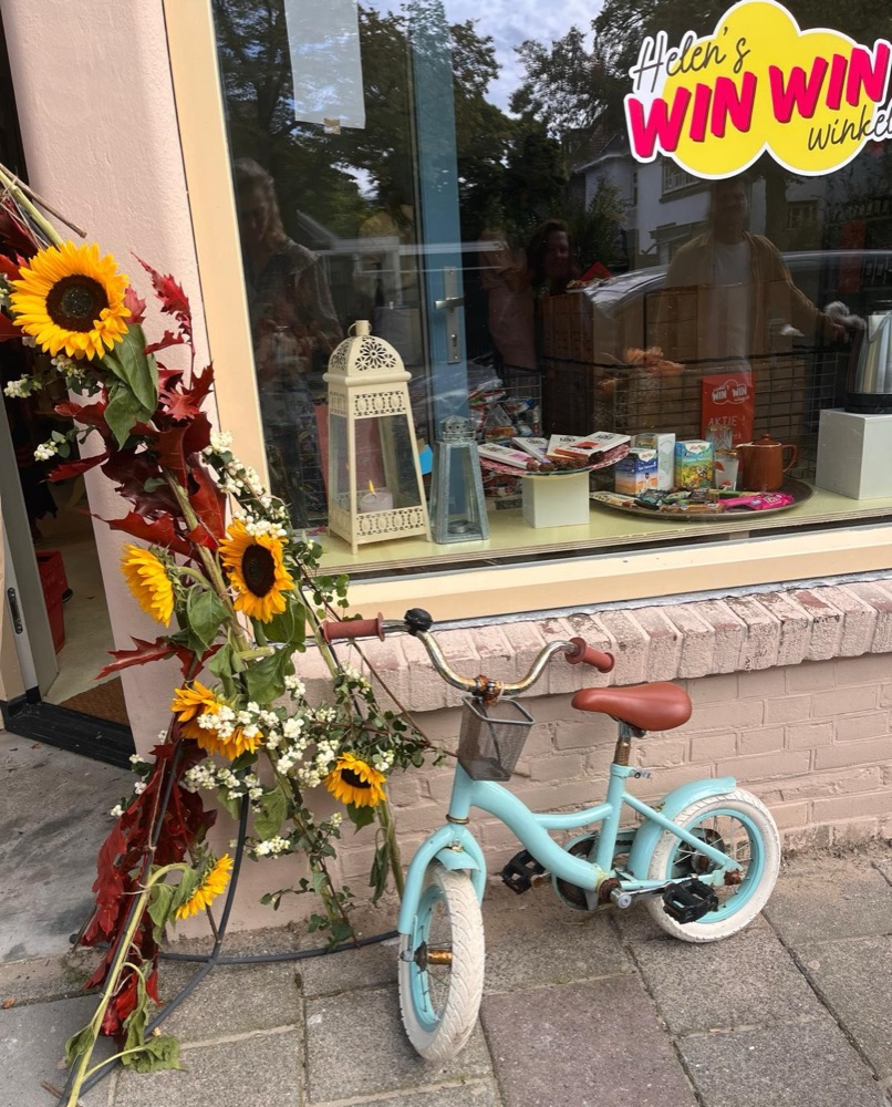 De gevel van de winkel met zonnebloemen en een kinderfietsje voor het raam